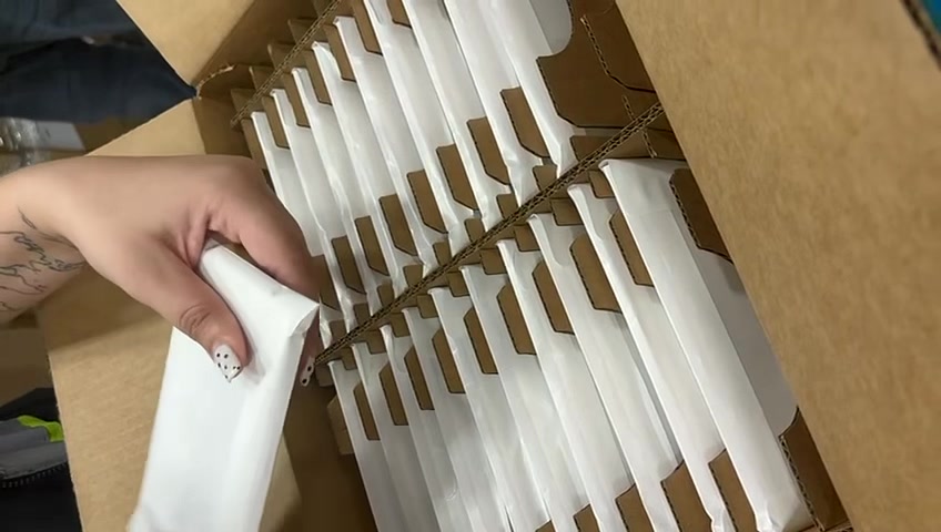 An opened master carton with rows of phones in white sleeves, one being lifted out